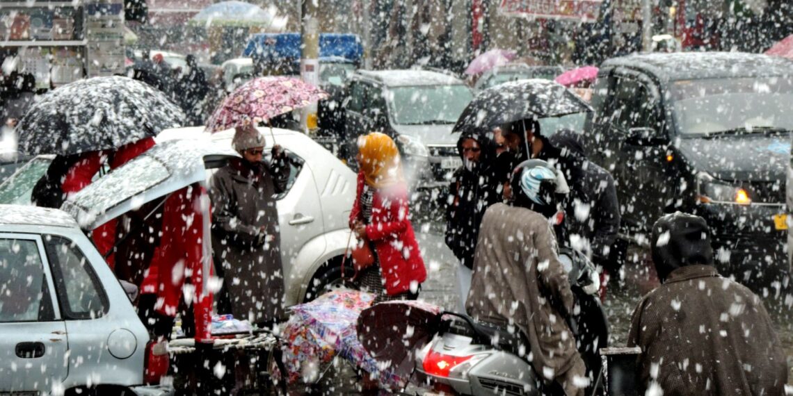 People shelter themselves under umbrellas as Srinagar experienced fresh snowfall on Monday