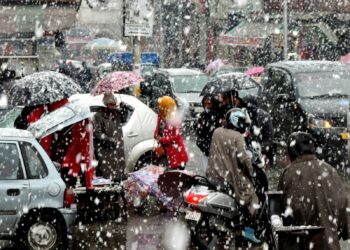 People shelter themselves under umbrellas as Srinagar experienced fresh snowfall on Monday