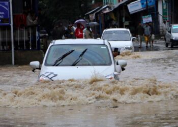 Commuters wade through water-logged road after heavy rain, on Wednesday