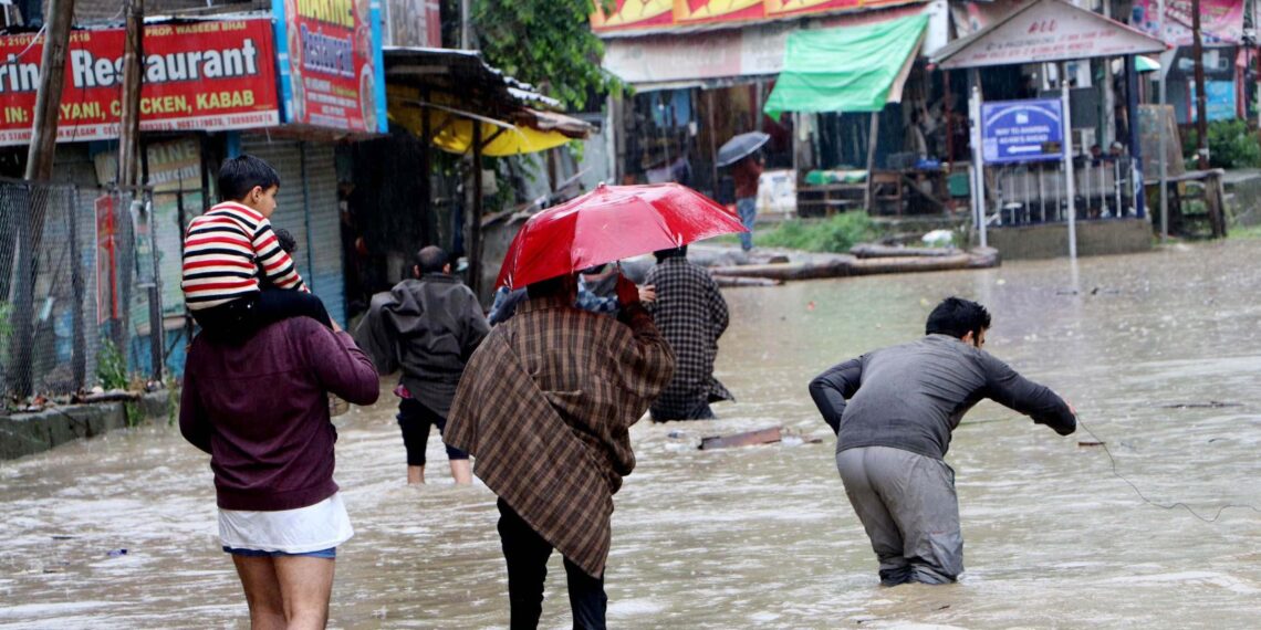 Commuters wade through water-logged road after heavy rain, on Wednesday