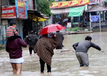 Commuters wade through water-logged road after heavy rain, on Wednesday